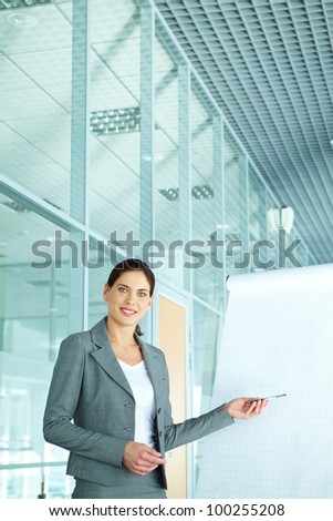 A beautiful businesswoman pointing at whiteboard and looking at camera