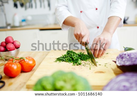 Chef cutting greenery on wooden board in the kitchen while cooking vegetarian food