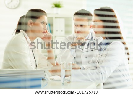 Unhappy female patient sitting in the doctors office, practitioners taking care of her