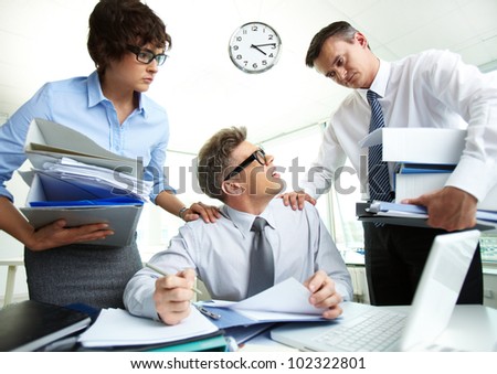 Perplexed accountant looking at his partner holding huge piles of documents