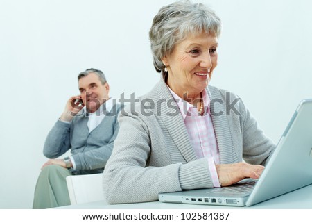 Portrait of senior woman typing with a man speaking on the phone on background