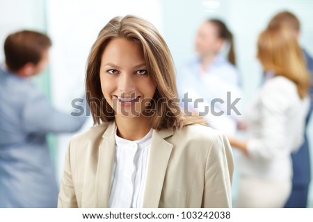 Portrait of pretty business woman looking at camera with working partners on background