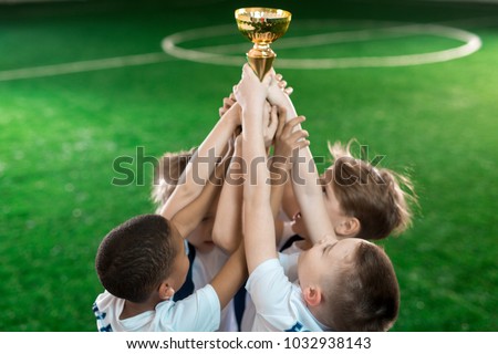 Group of young football champions raising hands with gold award