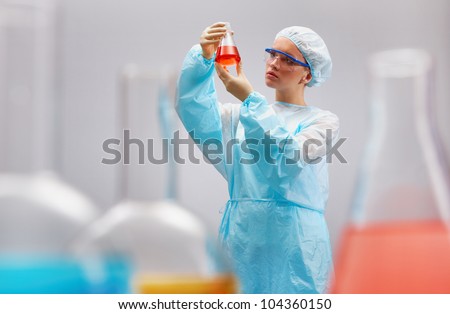 Girl in uniform of scientist holding a beaker and looking at its contents