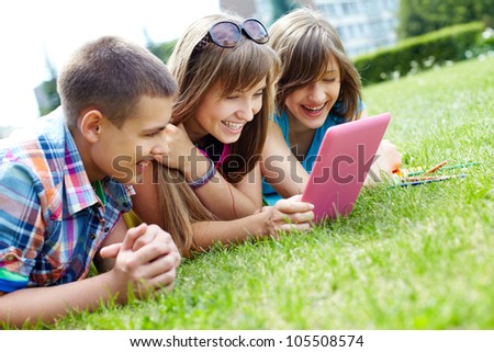 Girls and their male friend enjoying summer warmth and laughing at the sight of funny pictures on the pad screen