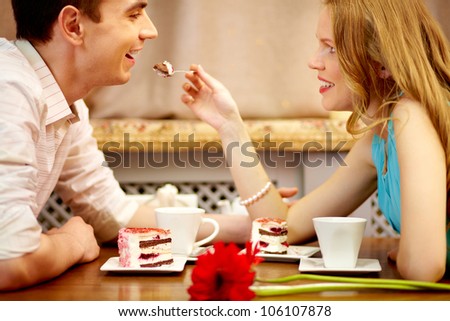 Young people sitting in the cafe and eating dessert, girl shares the cake with her boyfriend