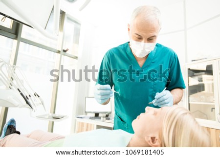 Professional dentist in uniform leaning over his patient before check-up with instruments