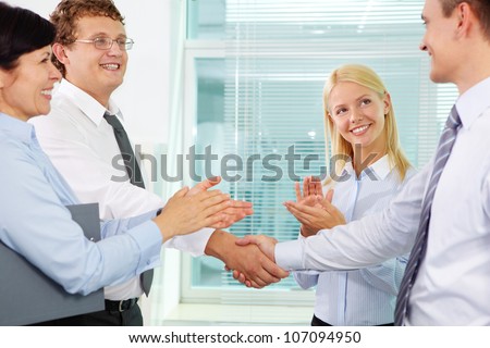 Successful businessmen handshaking while two females applauding after signing new contract