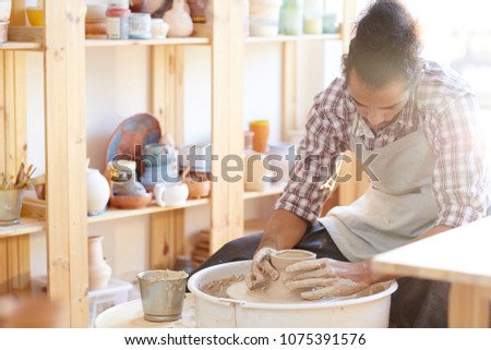 Young professional African American craftsman sitting in workshop and making clay ware on pottery wheel