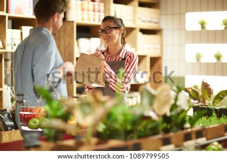 Happy shop assistant giving paper pack to man who chose something in supermarket