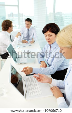 Young woman listening to experienced employee explaining her computer terms