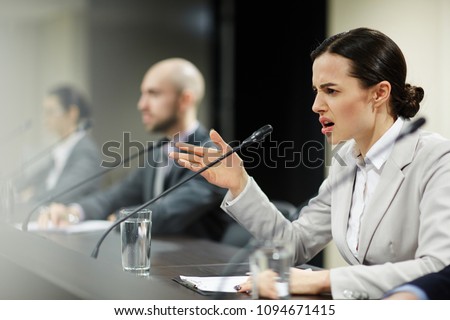 Indignant young female politician shouting into microphone at conference or political summit