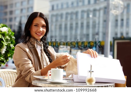Image of happy female in open air cafe taking out gift out of box outdoors
