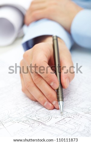Close-up of engineer hand with pen over blueprint with sketches of projects