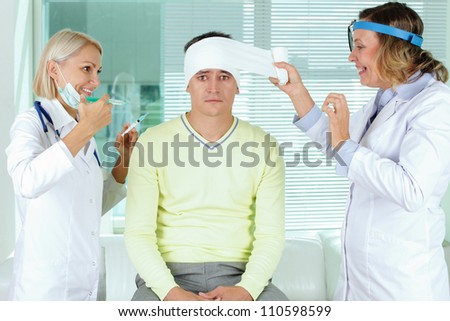 Portrait of two careful female doctors giving first aid to male patient in hospital