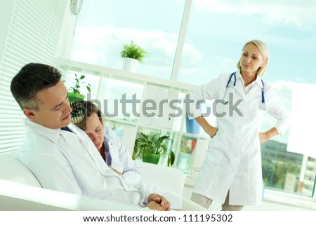 Tired clinicians in white coats sleeping in office while displeased doctor looking at them