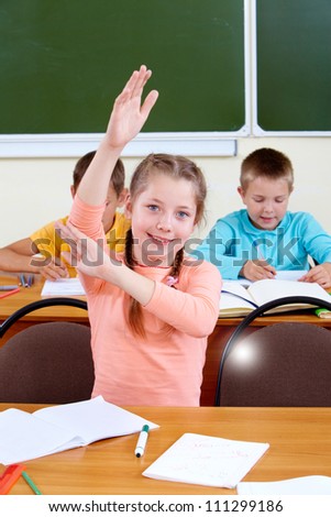 Portrait of lovely girl raising hand at workplace with schoolboys on background