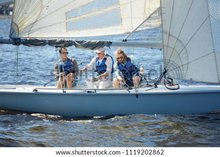 Group of active buddies in lifejackets sailing on yacht in open sea during summer voyage