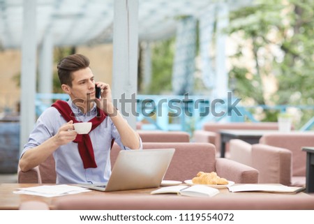 Busy man with smartphone and cup of tea having break in outdoor cafe in the middle of the day
