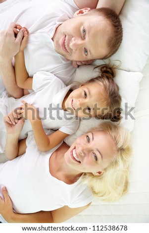 Above angle of happy parents and daughter lying on bed