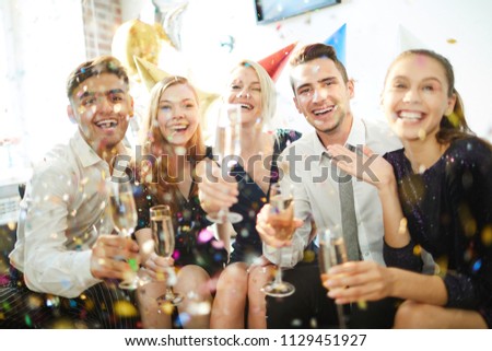 Young joyful friends with flutes of champagne having fun in confetti rain at birthday party