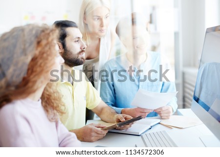 Group of four creative people watching webcast for designers while sitting in front of computer monitor