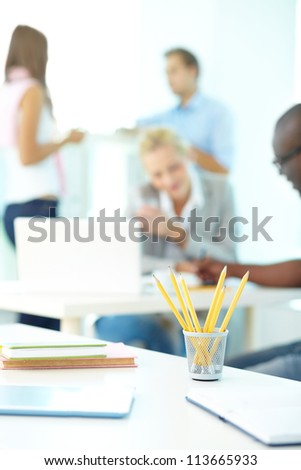 Close-up of several pencils in plastic glass on background of group of students working