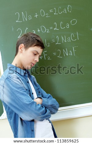 Sad guy standing by the blackboard with chemical formulae on it