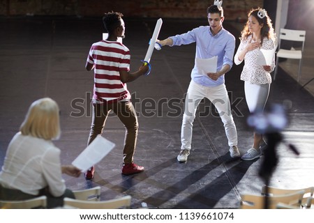 Two young princes fighting with paper swords for heart of princess during stage repetition