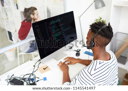 Serious busy African-American IT engineer in hands free device solving problem remotely and working with computer in office
