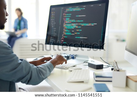 Computer programming specialist working on desktop computer and composing web code while carrying out task from order in office