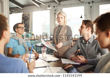 Team of creative business people discussing work at meeting table, focus on blonde female boss giving instructions to colleagues