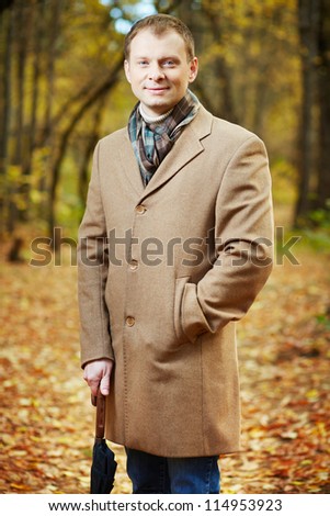 Portrait of elegant young man in coat looking at camera in autumn