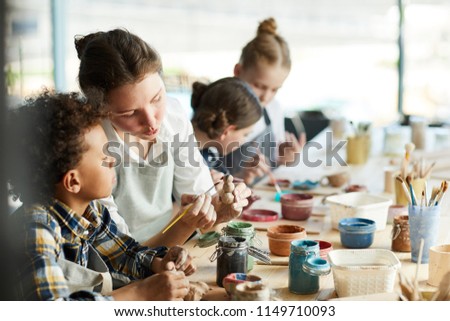 Young teacher showing one of pupils clay item and giving advice about painting it