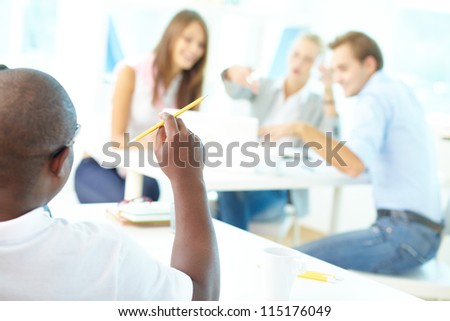 Rear view of African guy holding pencil with group of students working on background