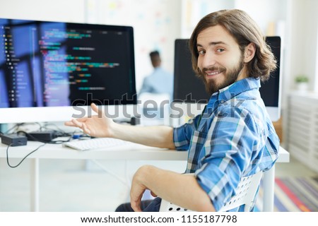 Young successful specialist in data decoding sitting by workplace and pointing at computer monitor