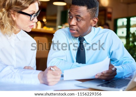 Black man sitting with executive woman at table exploring paper documents and working together