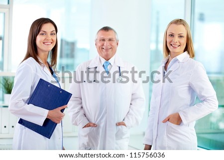 Portrait of female clinicians looking at camera with senior doctor on background