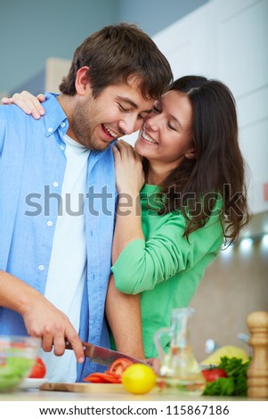 Portrait of young man cooking salad and his wife embracing him in the kitchen