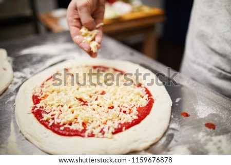 Raw rolled pizza dough with tomato ketchup and grated cheese on its top with human hand above