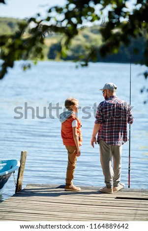 Rear view of father and his son standing on pier and are going to fish