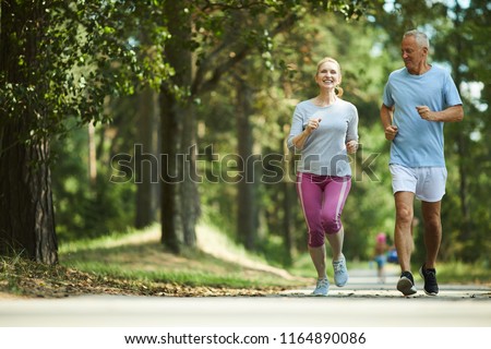 Active and healthy aged couple running in natural environment on summer morning