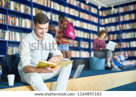 Young male student sitting with coffee and book at college library, he is preparing for exam