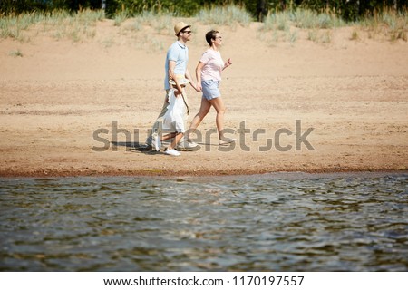 Side view portrait of modern happy family walking along edge of water on beach, copy space