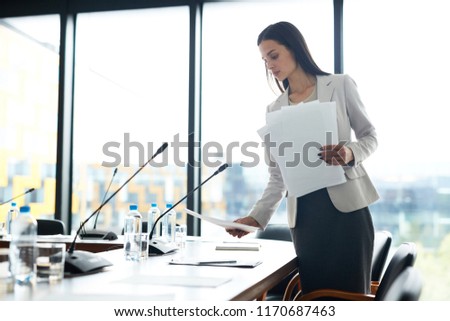 Portrait of elegant businesswoman placing papers on meeting table while prepairing conference room, copy space