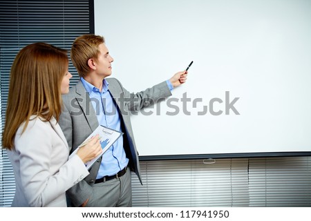 Confident businessman pointing at whiteboard while making speech with smart secretary near by