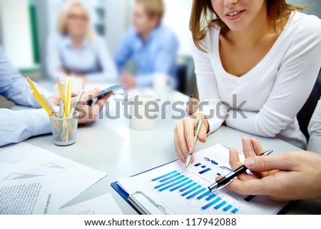Close-up of business partners hands over document with their colleagues working on background Close-up of business partners hands over document with their colleagues working on background