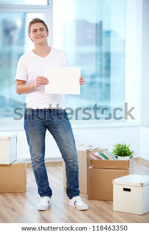 A young guy showing blank paper in new flat surrounded with boxes