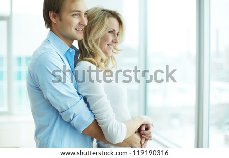 Image Of Young Guy Embracing His Girlfriend And Both Looking Through Window