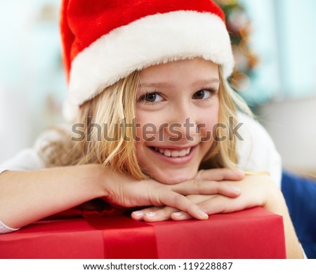 Portrait of cheerful girl with red giftbox looking at camera on Christmas evening